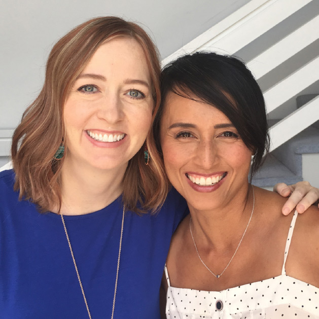 Two smiling women posing for a friendly photo, one wearing a blue top and the other in a polka-dot dress.